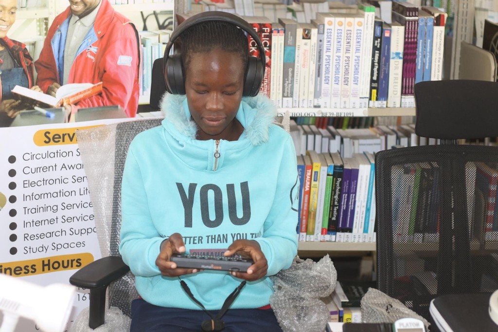 Student using HumanWare assistive technology with headphones in the library